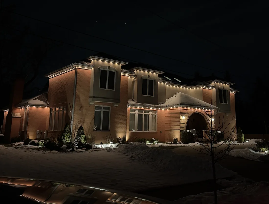 Warm white Christmas lights along the roofline of a snowy home in the North Shore