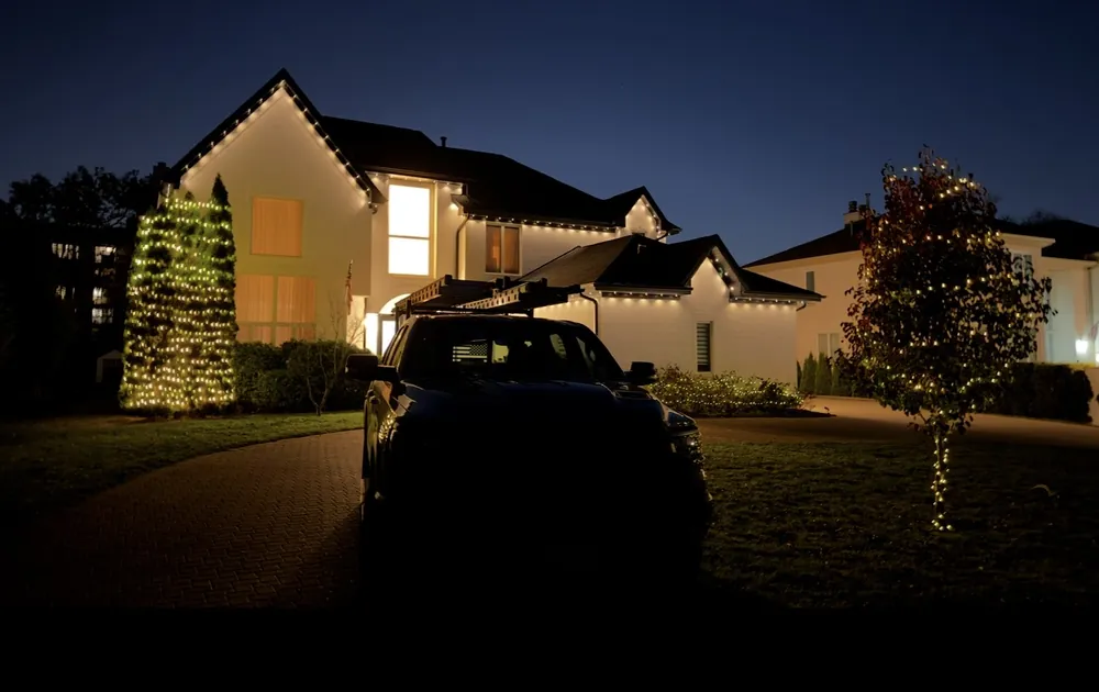 Warm white roofline Christmas lights and wrapped trees on a two-story home at dusk in Wheeling, IL - Perfect Touch