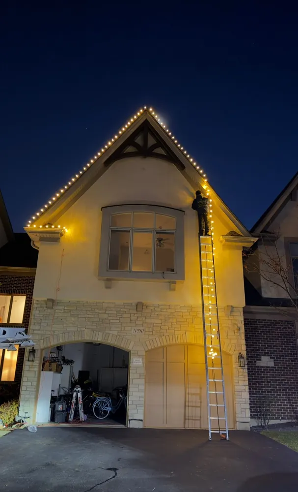 Perfect Touch installer hanging warm white Christmas lights on a gable roofline in Wheeling, IL